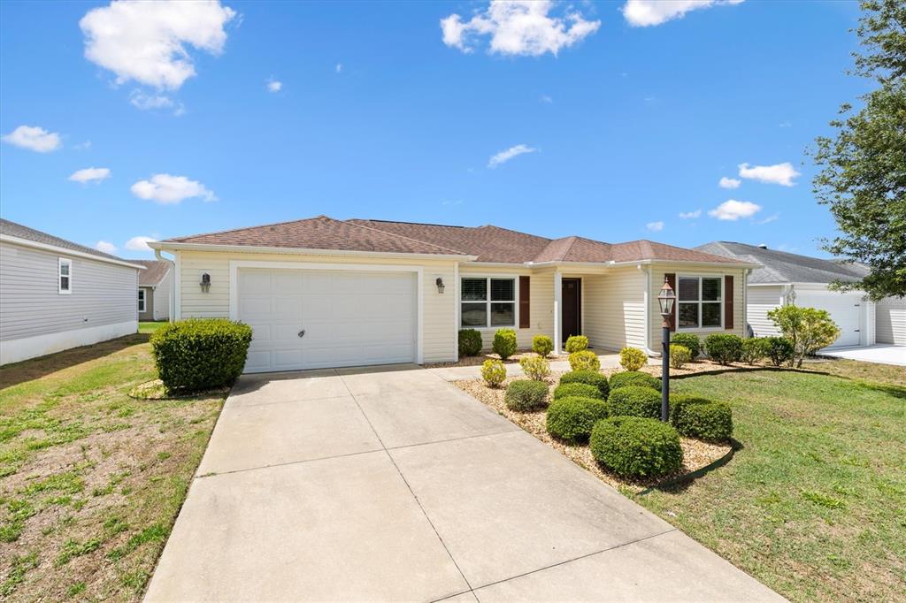 A single-story house with light siding, a two-car garage, and a landscaped front yard — 712 SHELTON STREET, THE VILLAGES, FL