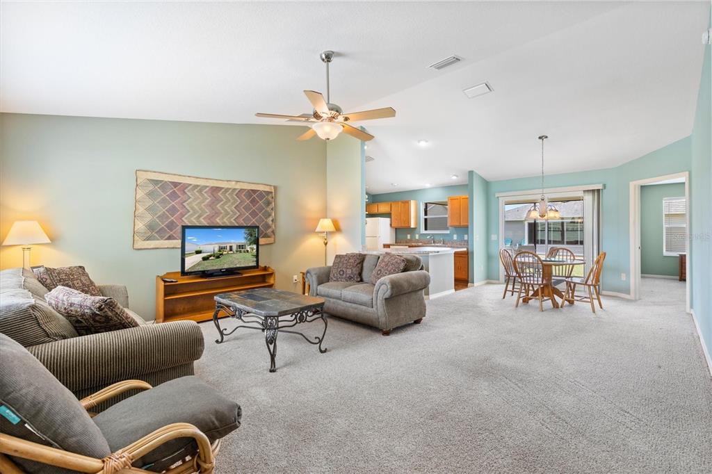 A living room with carpeted floors, a ceiling fan, and an open kitchen in the background — 712 SHELTON STREET, THE VILLAGES, FL
