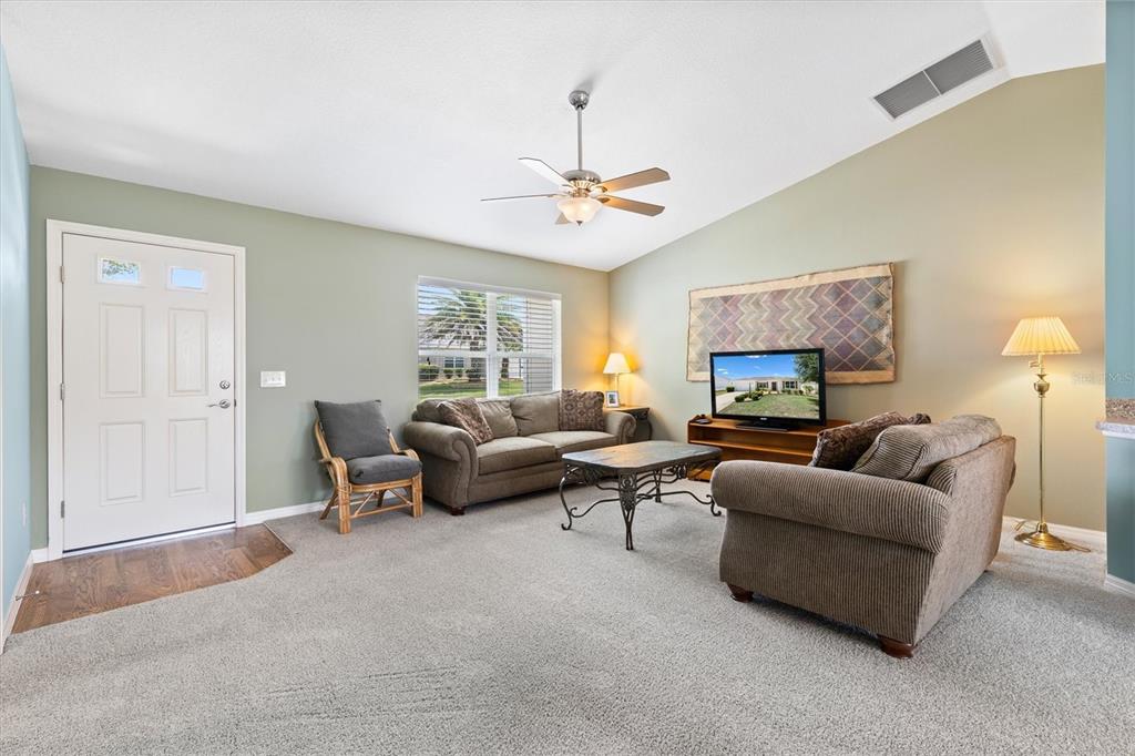 A living room features carpeted flooring, a ceiling fan, a sofa, and a television — 712 SHELTON STREET, THE VILLAGES, FL