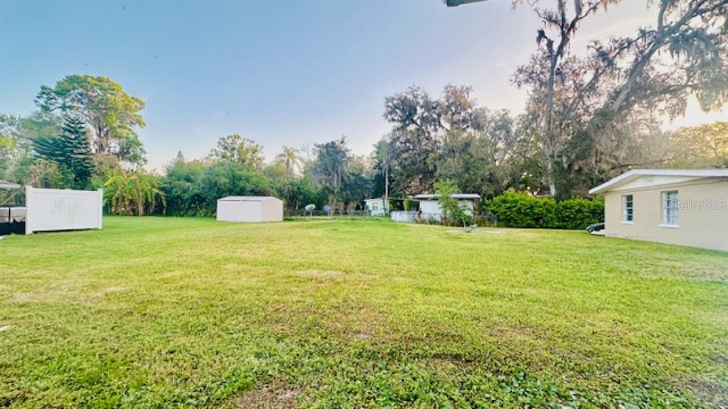 A large, grassy backyard features a white shed, a white fence, and a beige house — 101 ELLISON AVENUE, NEW SMYRNA BEACH, FL