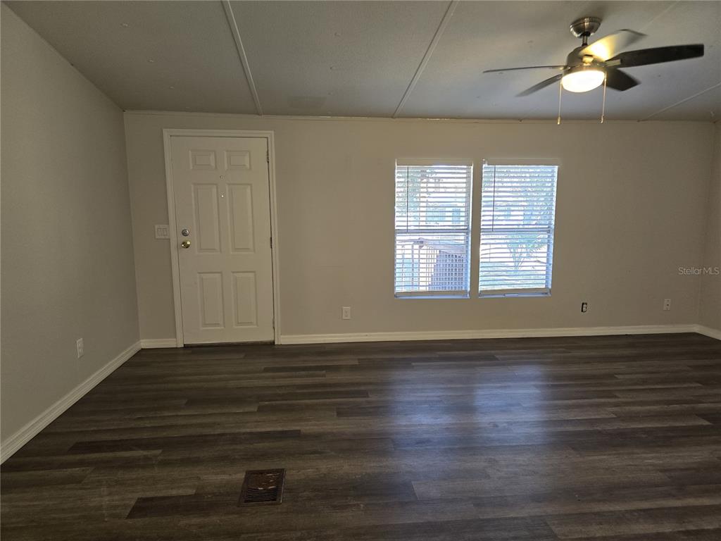 An empty living room features gray wood-look flooring, a white door, and a ceiling fan — 8013 FORMBY STREET, RIVERVIEW, FL