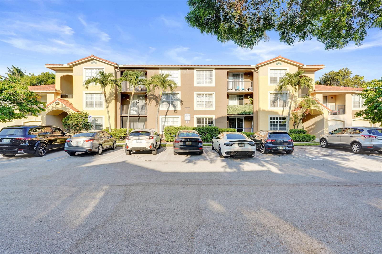 A three-story apartment building with a parking lot in front and several parked cars — 15075 Michelangelo Boulevard # 103, Delray Beach FL 33446, DELRAY BEACH, FL