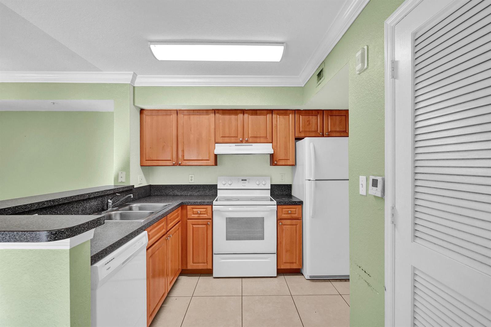 A kitchen with light green walls, wood cabinets, white appliances, and dark laminate countertops — 15075 Michelangelo Boulevard # 103, Delray Beach FL 33446, DELRAY BEACH, FL
