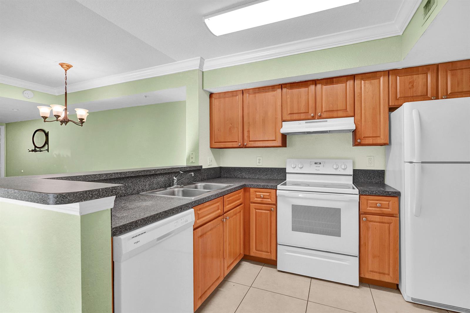 A kitchen with light wood cabinets, dark countertops, white appliances, and light green walls — 15075 Michelangelo Boulevard # 103, Delray Beach FL 33446, DELRAY BEACH, FL