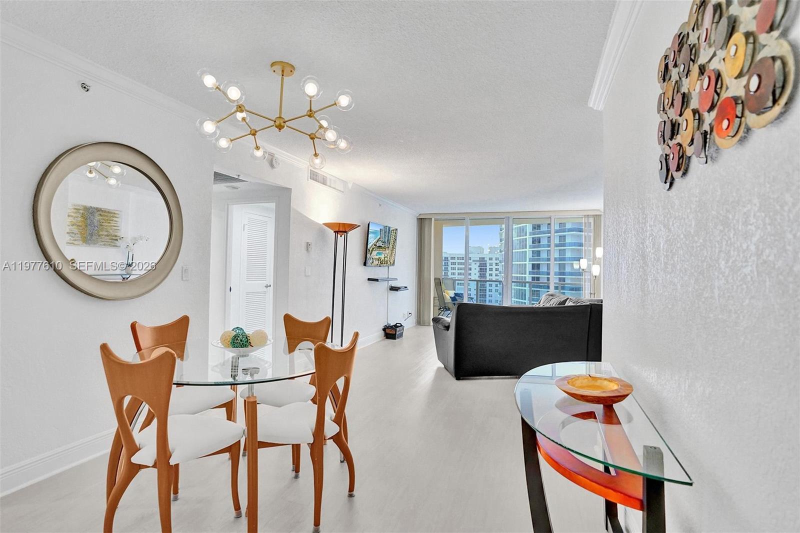 A dining area with a glass table and modern chandelier opens into a living room — 2501 S Ocean Dr, Hollywood FL 33019, HOLLYWOOD, FL