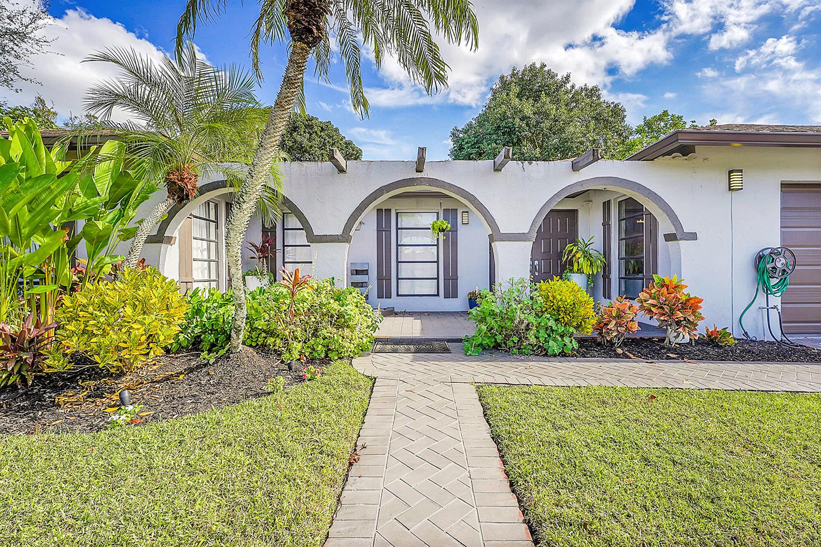 A white house with three arched entryways and a brick walkway leading to the front door — 1618 The 12th Fairway, Wellington FL 33414, WELLINGTON, FL