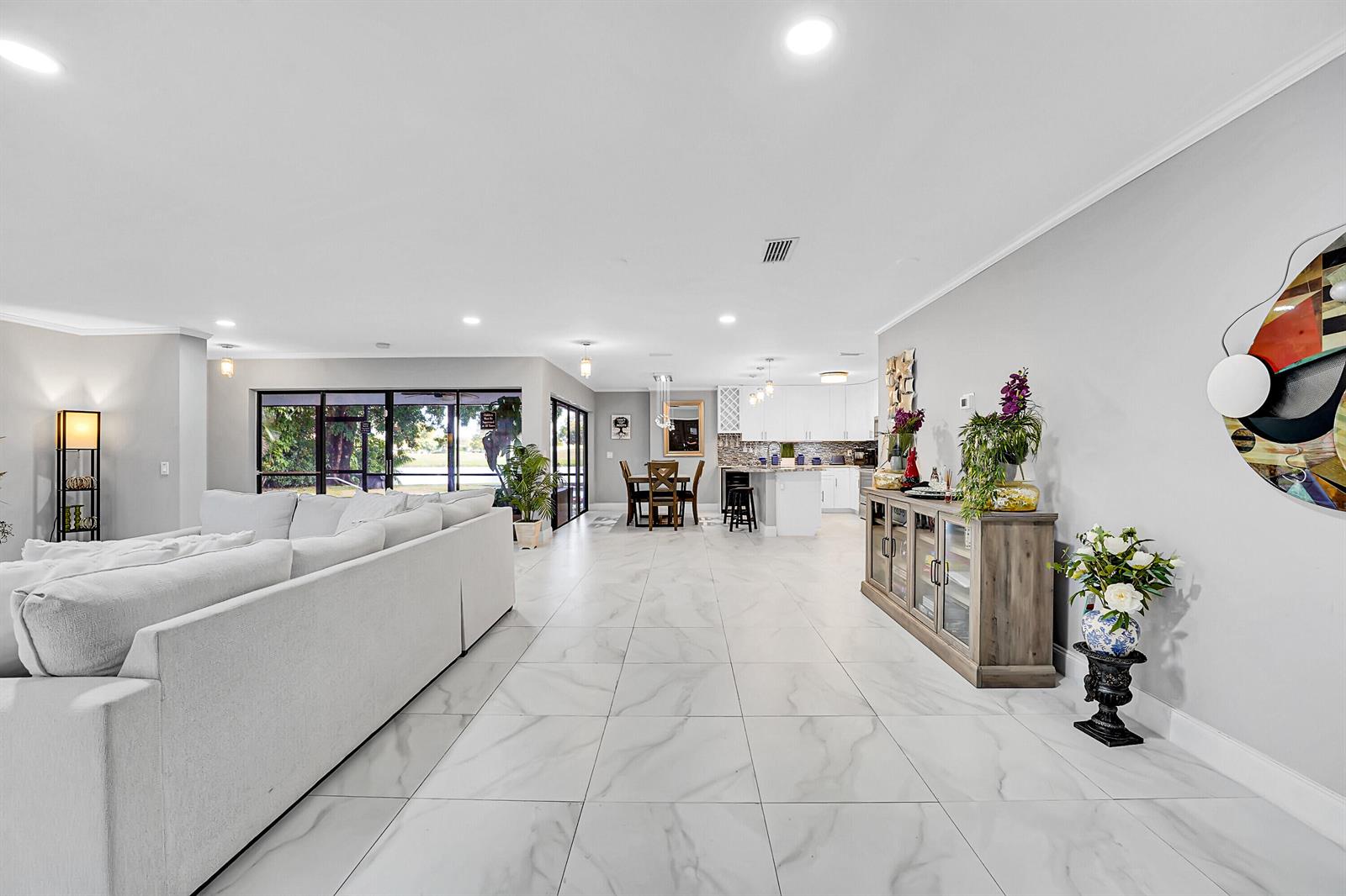 An open-concept living and dining area features white tile flooring, a large sofa, and kitchen — 1618 The 12th Fairway, Wellington FL 33414, WELLINGTON, FL