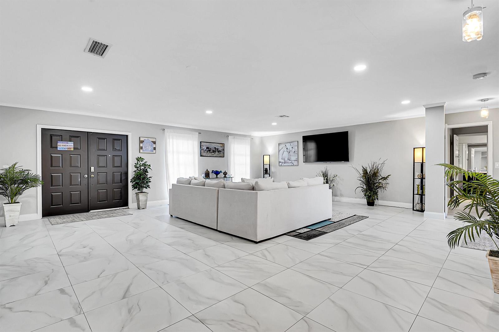 A spacious living room features white marble-look tile flooring, a large sectional sofa, and double doors — 1618 The 12th Fairway, Wellington FL 33414, WELLINGTON, FL
