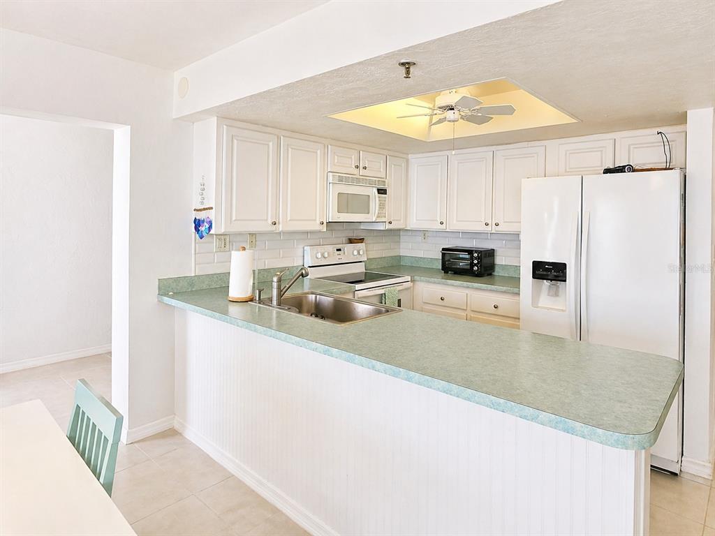 A kitchen features white cabinets, green laminate countertops, a white refrigerator, and a ceiling fan — 4141 S ATLANTIC AVENUE UNIT 406, NEW SMYRNA BEACH, FL