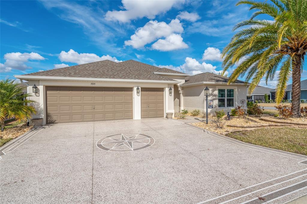 A single-story house with a three-car garage and a decorative compass rose on the driveway — 595 RANDALL ROAD, THE VILLAGES, FL