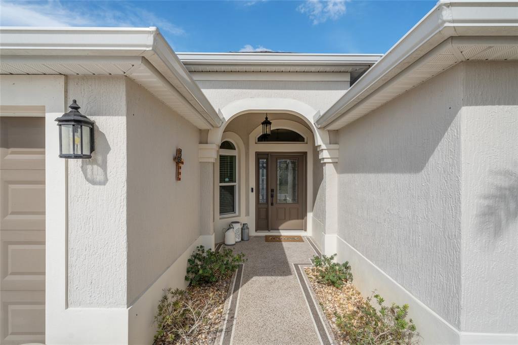 A beige stucco house exterior features a covered entryway with a brown front door — 595 RANDALL ROAD, THE VILLAGES, FL