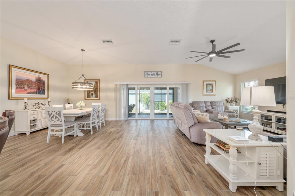 A bright open-concept living and dining area features wood-look tile flooring and sliding glass doors — 595 RANDALL ROAD, THE VILLAGES, FL