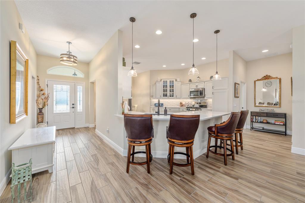 A kitchen with a breakfast bar and stools opens into a bright entryway with tile floors — 595 RANDALL ROAD, THE VILLAGES, FL