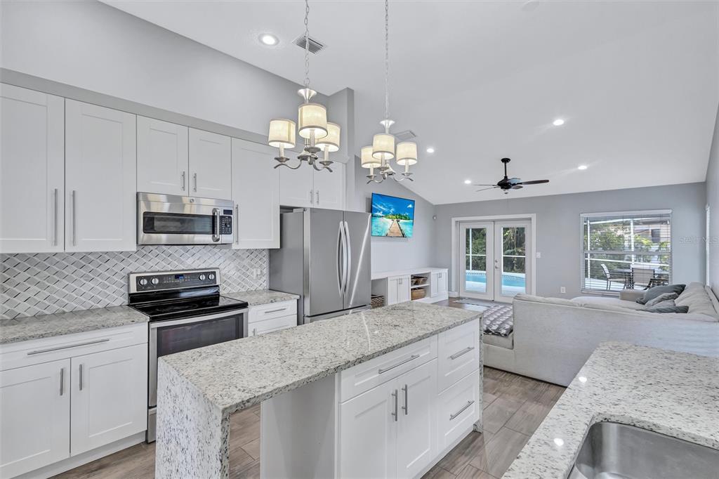 A modern kitchen with white cabinets, granite countertops, and an island overlooking a living area — 4909 6TH AVENUE E, BRADENTON, FL
