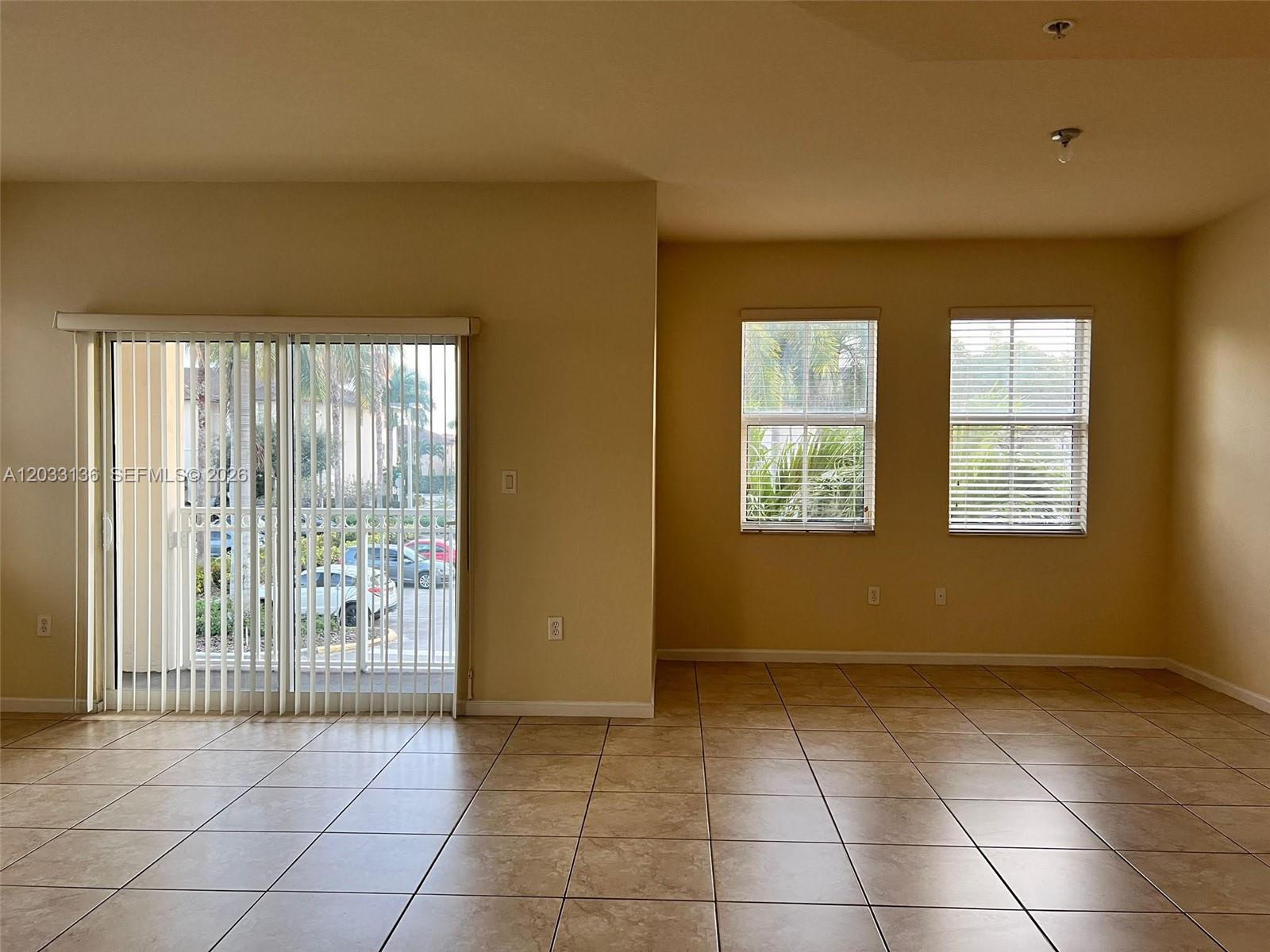 An empty room features beige walls, tile flooring, a sliding glass door, and two windows — 11503 NW 89th St # 223, Doral FL 33178, DORAL, FL