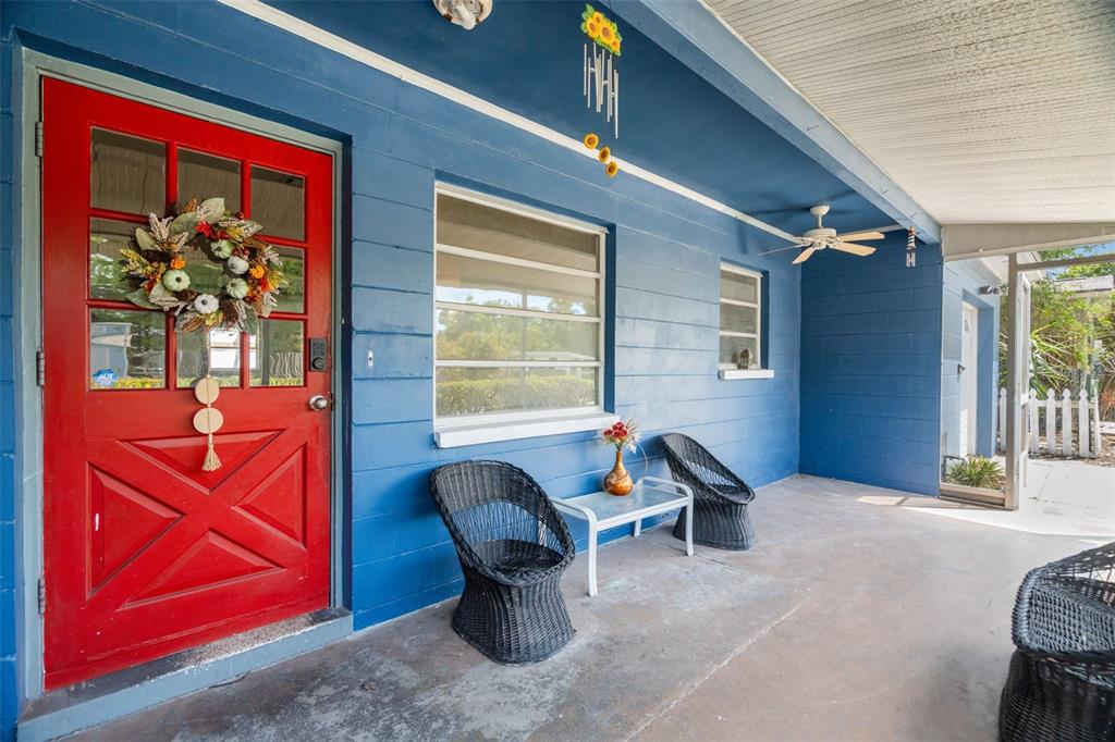 A blue exterior wall features a red front door and a covered porch with seating — 2027 E VALENCIA WAY E, CLEARWATER, FL