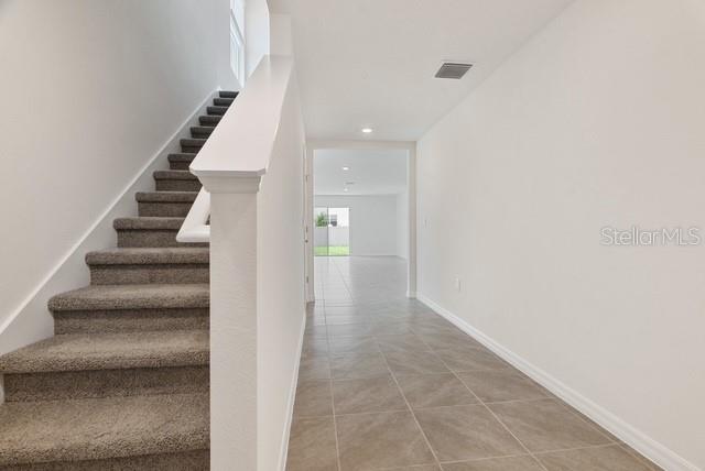 A carpeted staircase sits beside a tiled hallway leading toward a bright, open living space — 8686 SW 44TH TERRACE, OCALA, FL