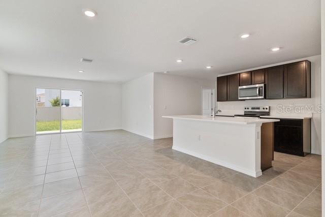 An open-concept kitchen with dark wood cabinets and a white island overlooks a tiled living area — 8686 SW 44TH TERRACE, OCALA, FL