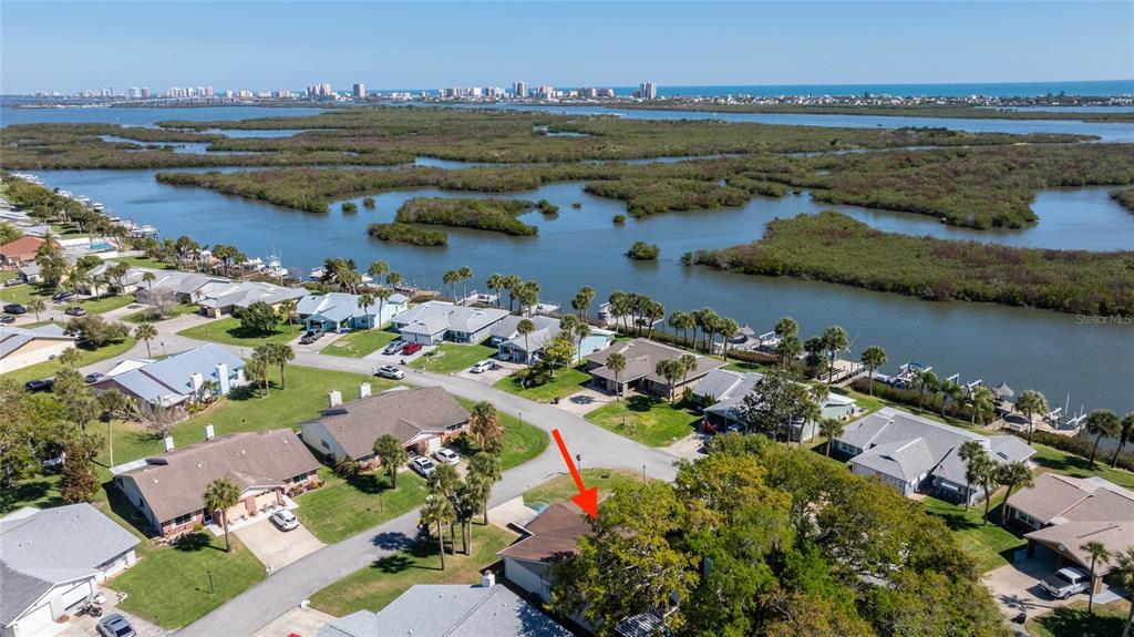 An aerial view shows a residential neighborhood with houses near a waterway and coastal skyline — 1402 PORTOBELLO DRIVE, PORT ORANGE, FL