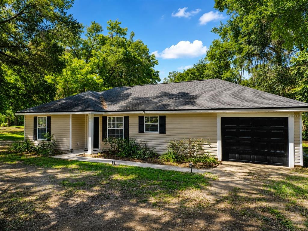 A single-story house with tan siding, black shutters, a dark roof, and a black garage door — 901 SW PECAN STREET, KEYSTONE HEIGHTS, FL