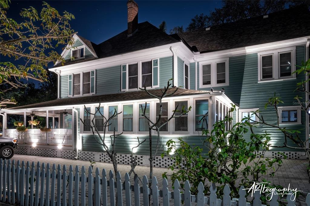 A two-story teal house with a wrap-around porch and white picket fence at night — 304 15TH STREET W, BRADENTON, FL