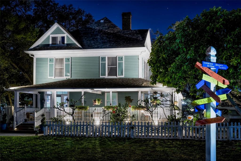 A two-story, light green Victorian-style house with a wraparound porch at night — 304 15TH STREET W, BRADENTON, FL