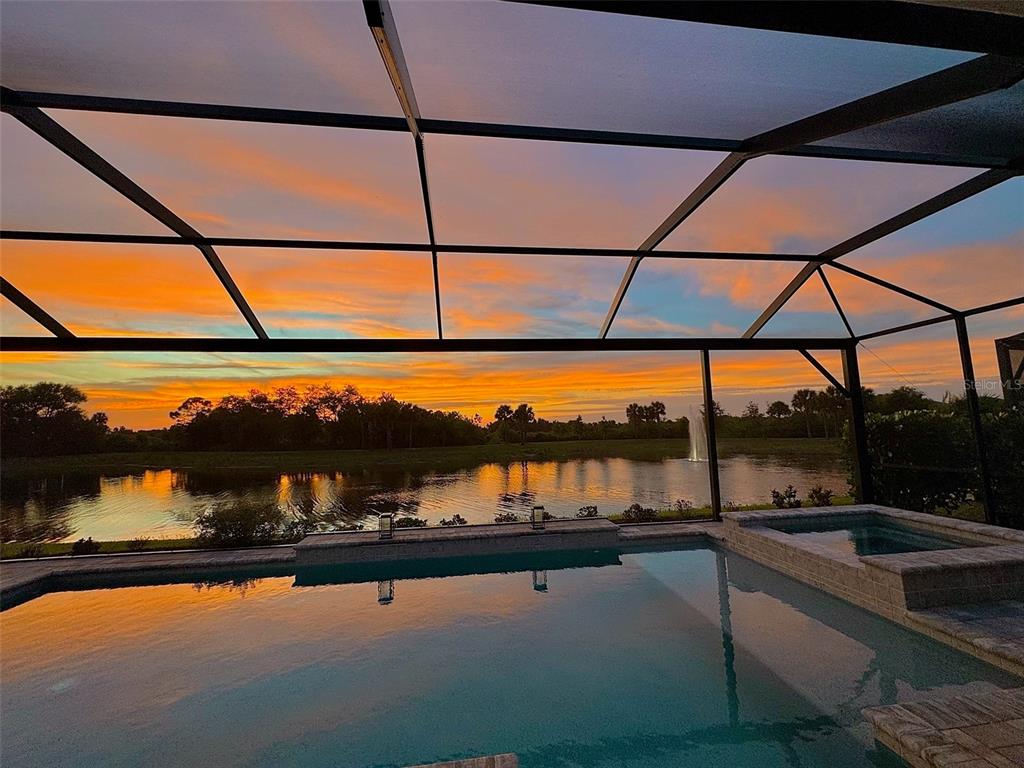 A swimming pool and spa are enclosed by a screen overlooking a lake at sunset — 18035 HOME RUN DRIVE, VENICE, FL