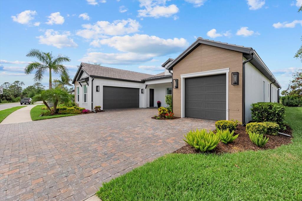 A single-story house with a paver driveway, two garages, and white vertical siding — 18035 HOME RUN DRIVE, VENICE, FL