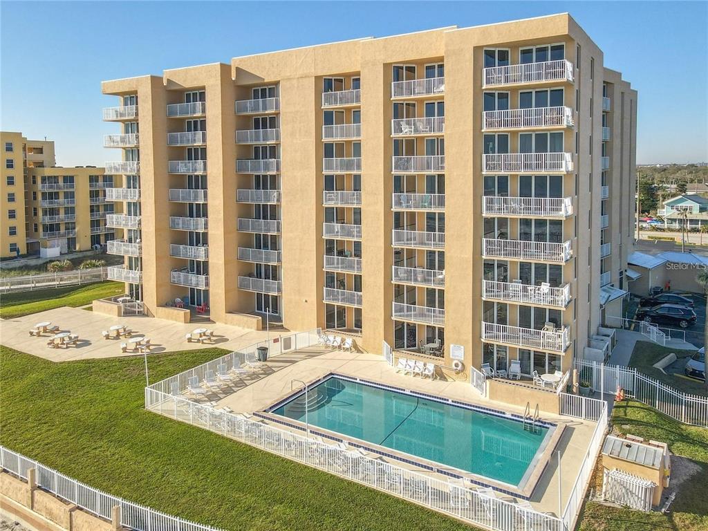 An aerial view of a multi-story tan apartment building with balconies and an outdoor pool — 421 S ATLANTIC AVENUE UNIT 409, NEW SMYRNA BEACH, FL
