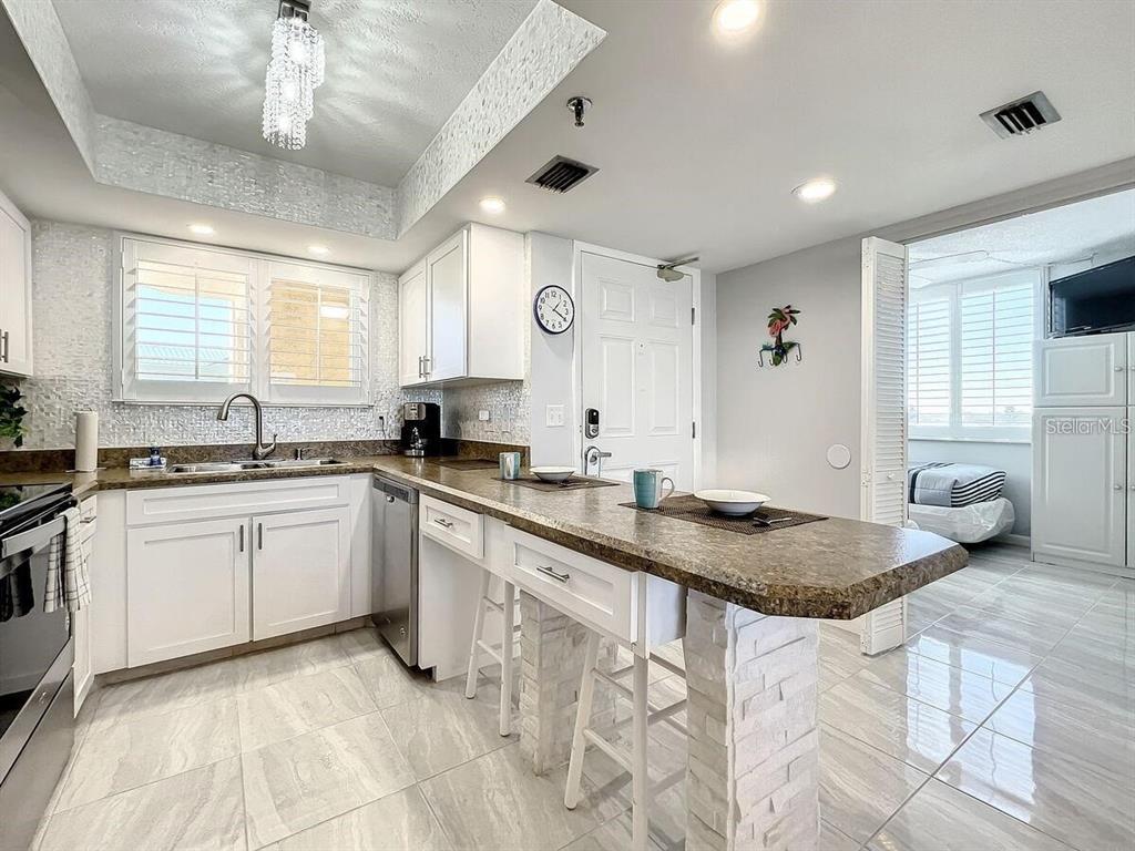 A kitchen features white cabinets, a stone-topped breakfast bar, and light tile flooring — 421 S ATLANTIC AVENUE UNIT 409, NEW SMYRNA BEACH, FL