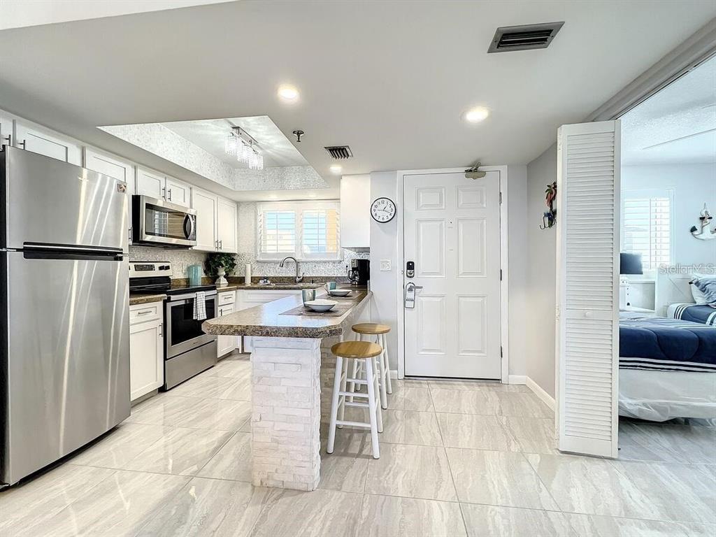A kitchen features stainless steel appliances, white cabinetry, a stone-topped breakfast bar, and tiled floors — 421 S ATLANTIC AVENUE UNIT 409, NEW SMYRNA BEACH, FL