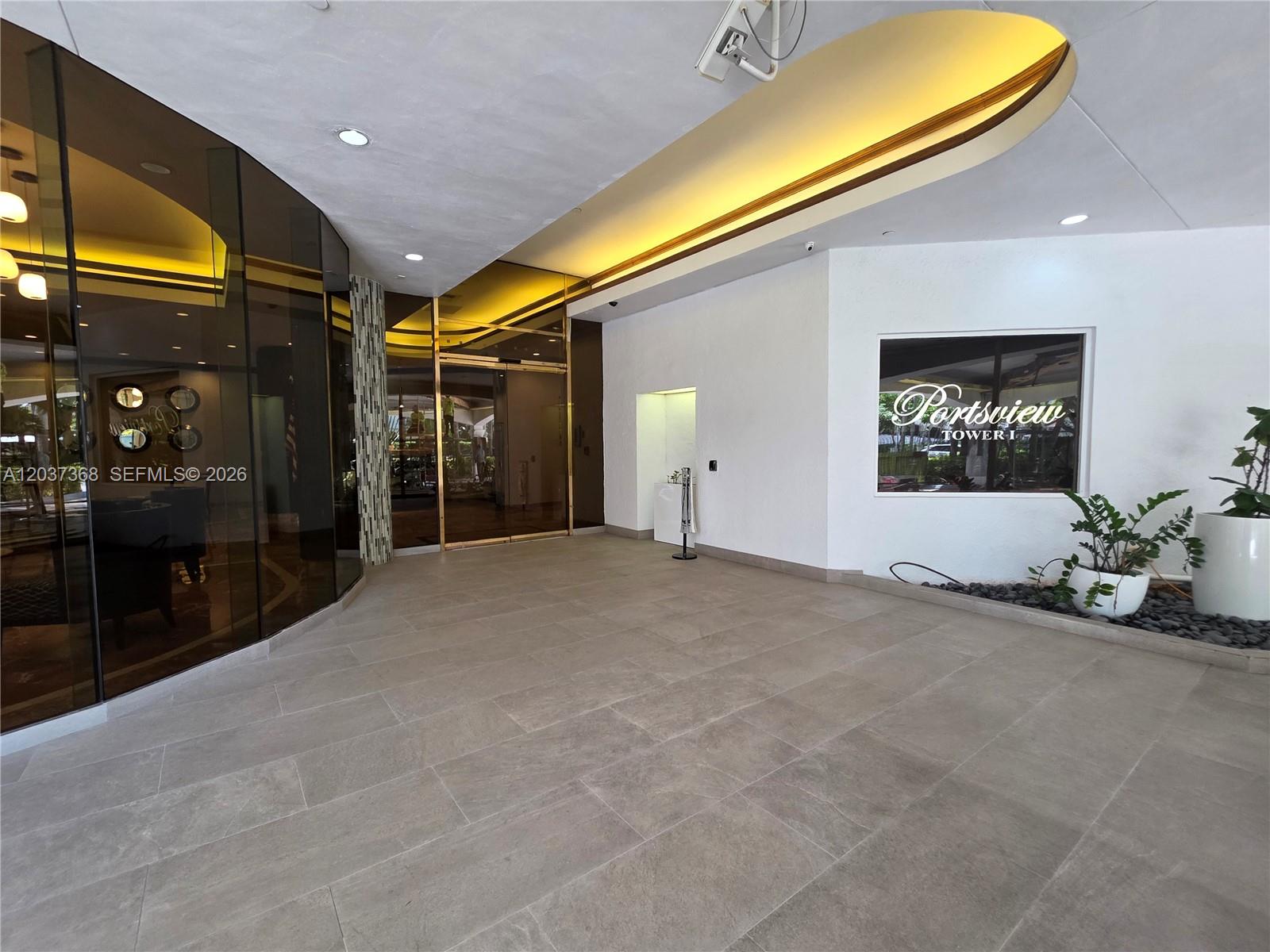 The lobby of a building features large glass walls, tile flooring, and a decorative ceiling — AVENTURA, FL