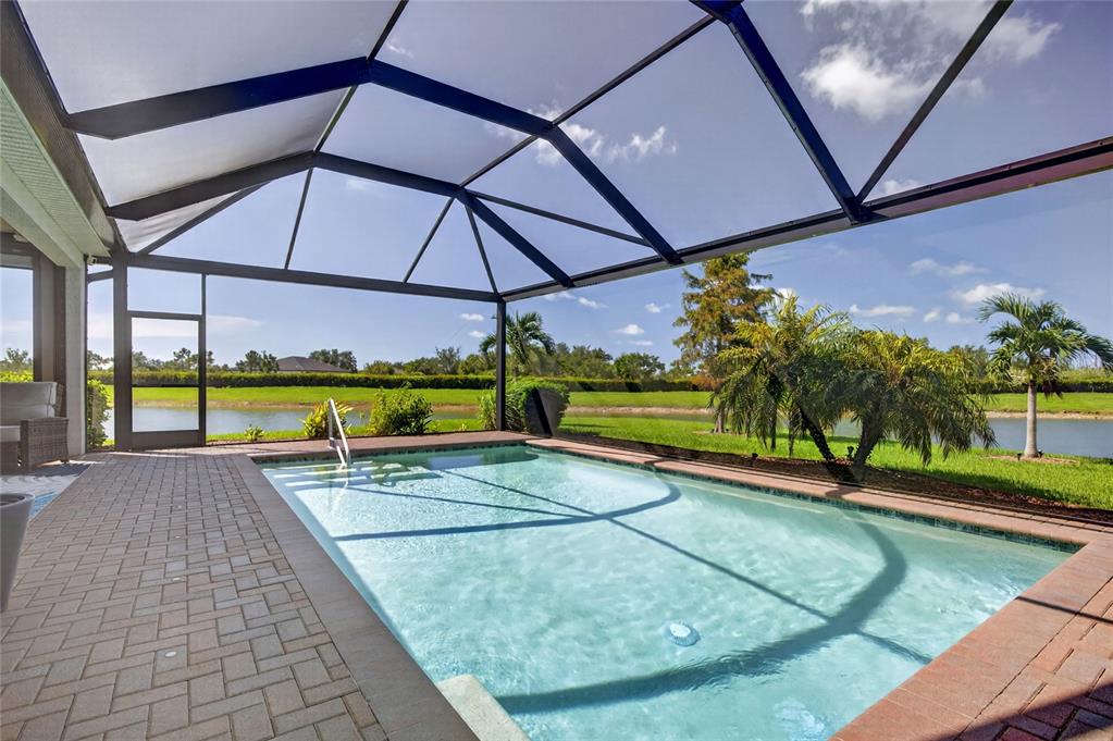 A screened-in swimming pool with a brick paver deck overlooking a pond and palm trees — 14605 PONCE DE LEON TRAIL, PORT CHARLOTTE, FL