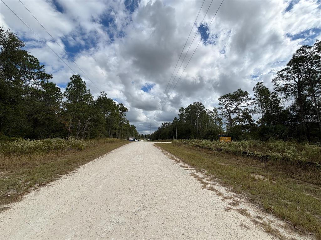 A gravel road stretches through a wooded area under a cloudy sky — Lot 11 RED MARLIN AVENUE, WEEKI WACHEE, FL
