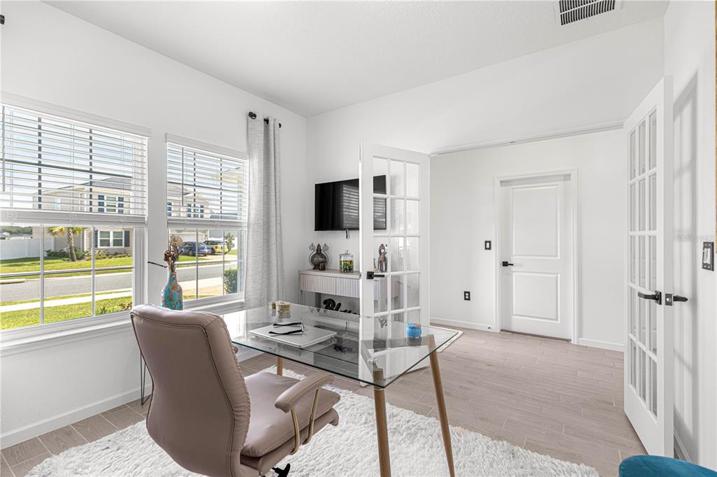 A home office features a glass desk, a plush rug, and French doors — 4417 NW 14TH LOOP, OCALA, FL