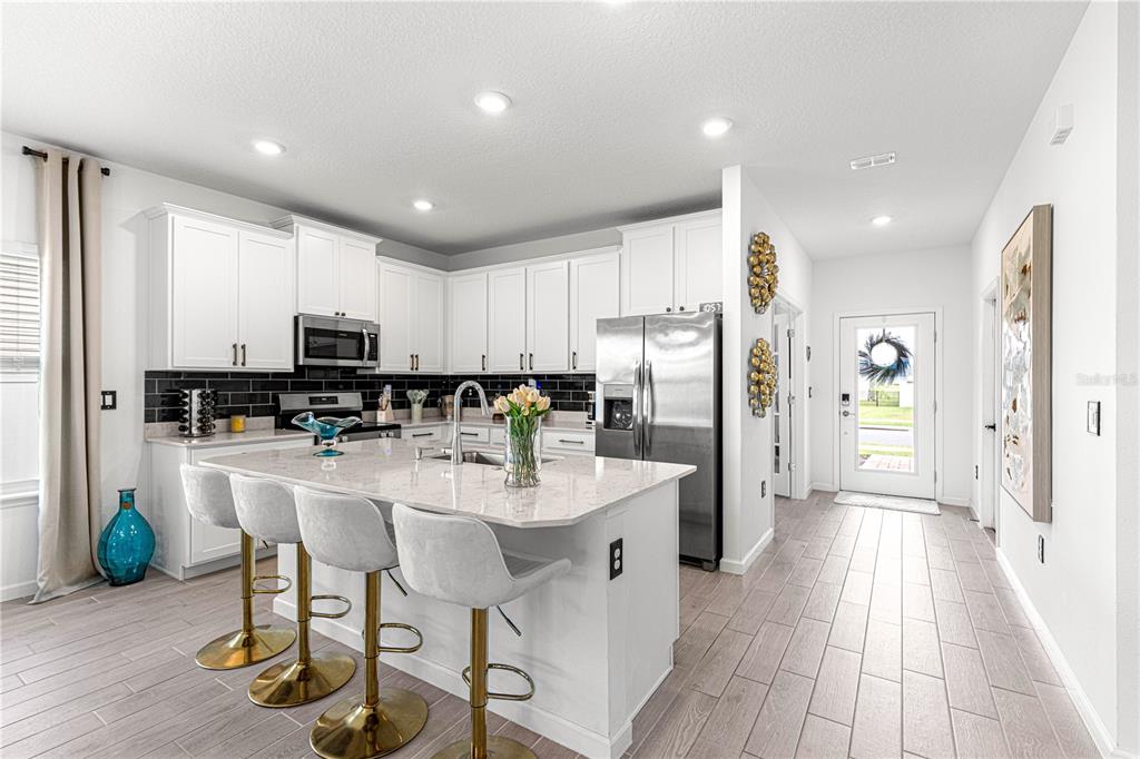 A modern kitchen features white cabinetry, a quartz island with barstools, and wood-look tile flooring — 4417 NW 14TH LOOP, OCALA, FL