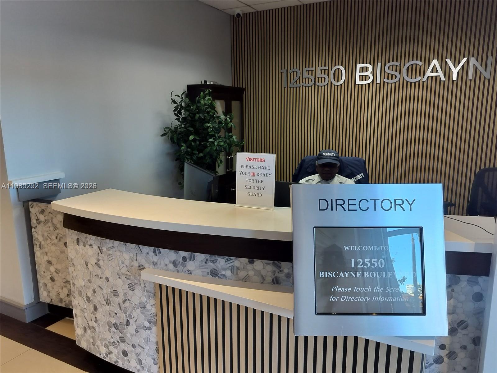 A security guard sits at a reception desk in a lobby with a directory kiosk — 12550 Biscayne Blvd # 213, North Miami FL 33181, NORTH MIAMI, FL