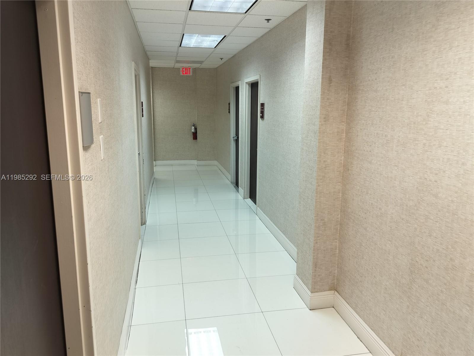 A brightly lit office hallway features white tile flooring, textured beige walls, and several doors — 12550 Biscayne Blvd # 213, North Miami FL 33181, NORTH MIAMI, FL