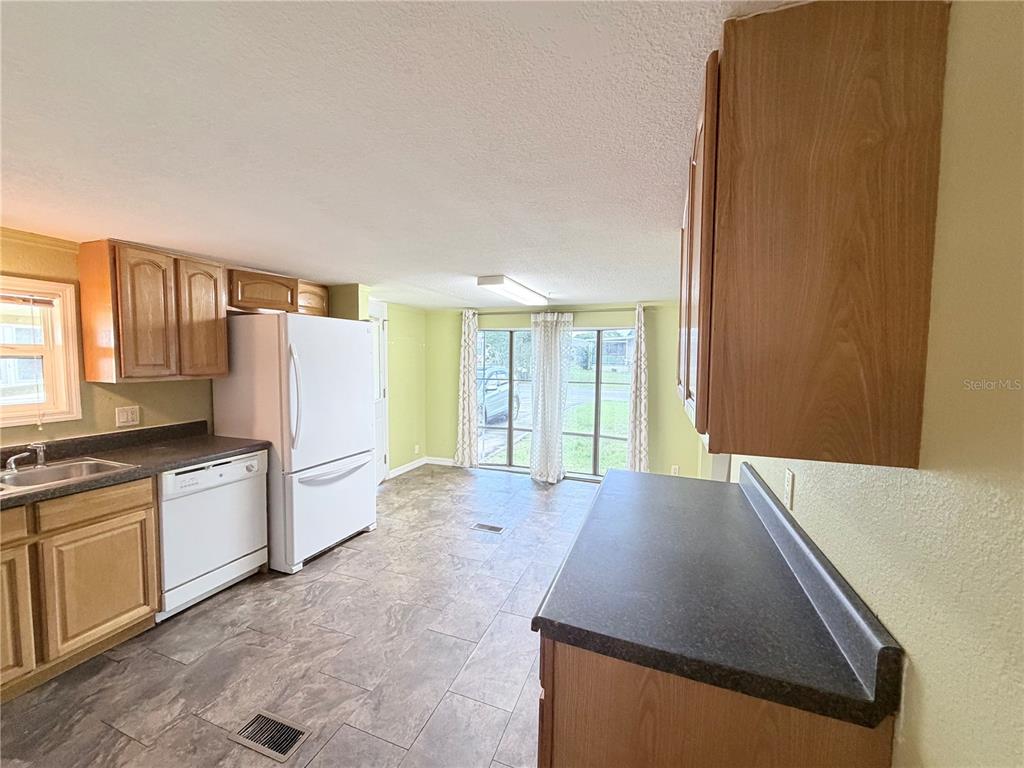 A kitchen with light wood cabinets, dark countertops, white appliances, and a tiled floor — 14224 SANDHURST STREET, BROOKSVILLE, FL