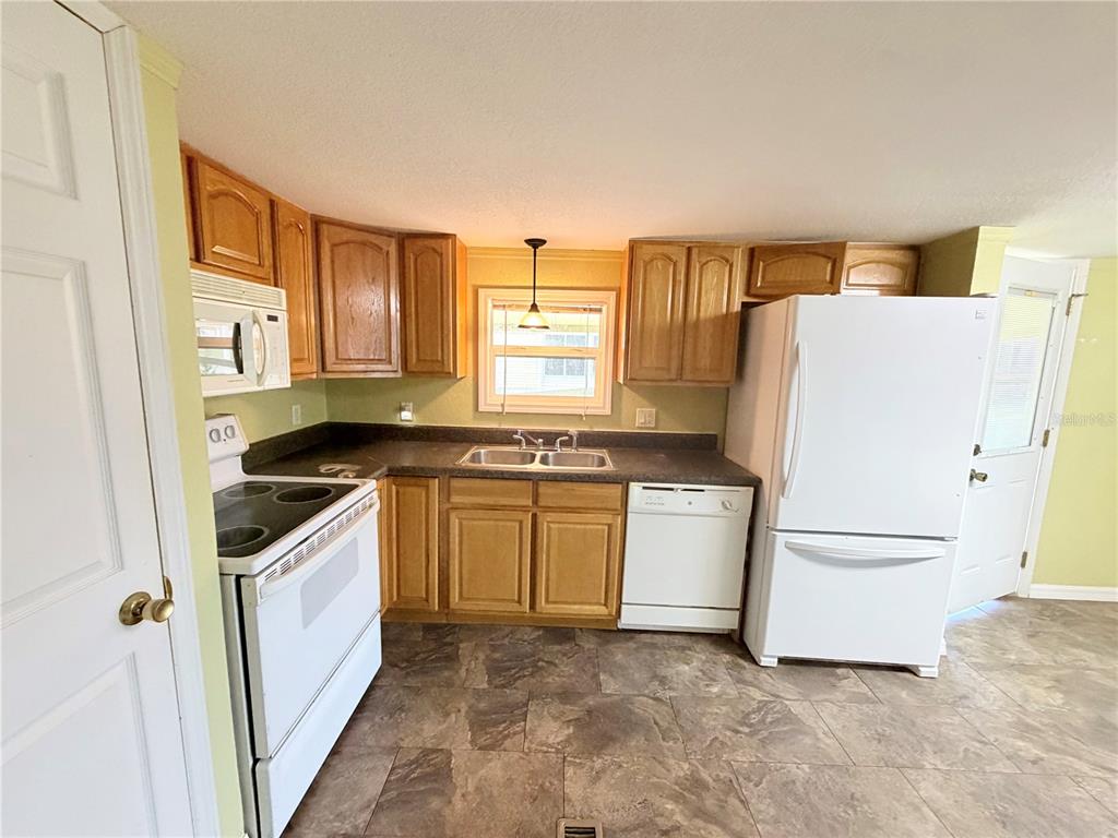 A kitchen features wood cabinets, white appliances, dark countertops, and a window above the sink — 14224 SANDHURST STREET, BROOKSVILLE, FL