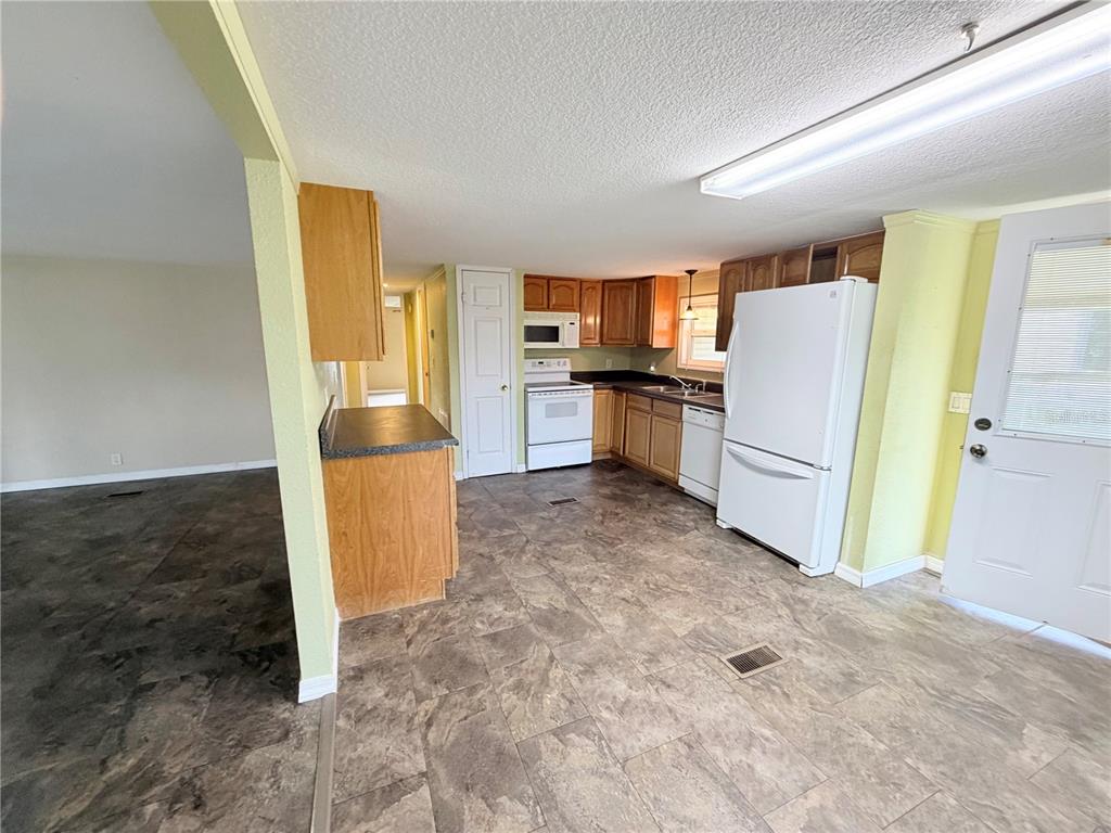 A kitchen with wood cabinets, white appliances, and tile flooring opens to an adjacent room — 14224 SANDHURST STREET, BROOKSVILLE, FL