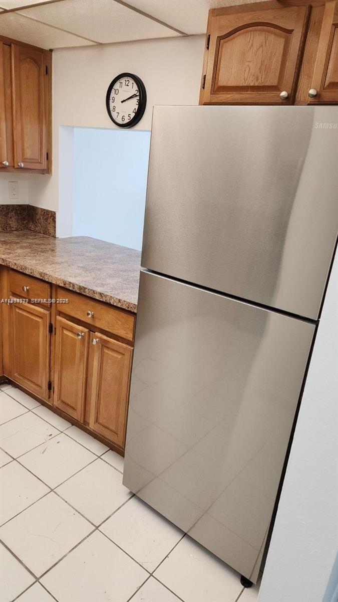 A kitchen features wooden cabinets, a stainless steel refrigerator, and a tiled floor — 10000 NW 80th Ct # 2415, Hialeah Gardens FL 33016, HIALEAH GARDENS, FL