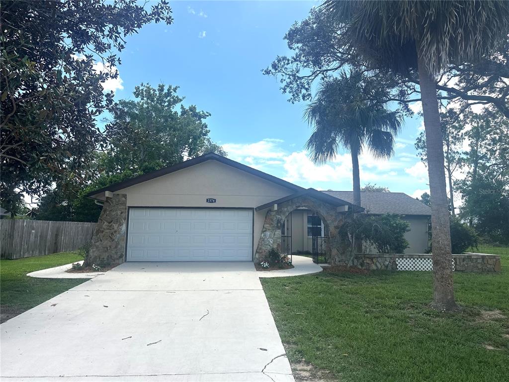 A single-story house features a stone-accented facade, a two-car garage, and a palm tree — 2378 CANFIELD DRIVE, SPRING HILL, FL