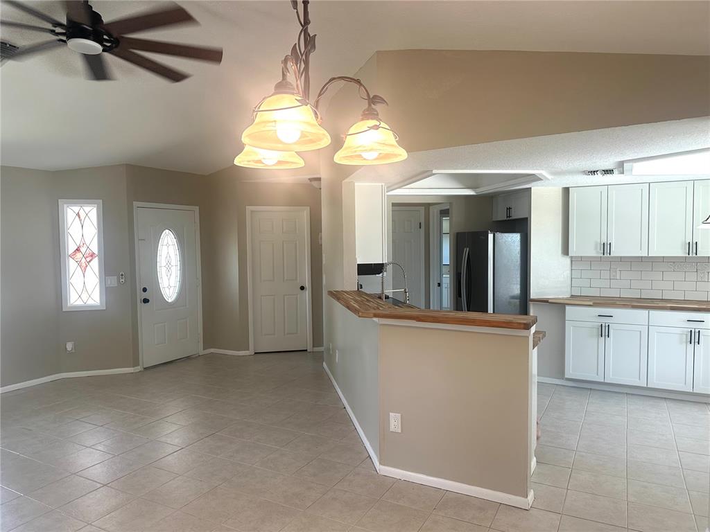 A kitchen with white cabinets and a wooden breakfast bar overlooks a tiled living area — 2378 CANFIELD DRIVE, SPRING HILL, FL