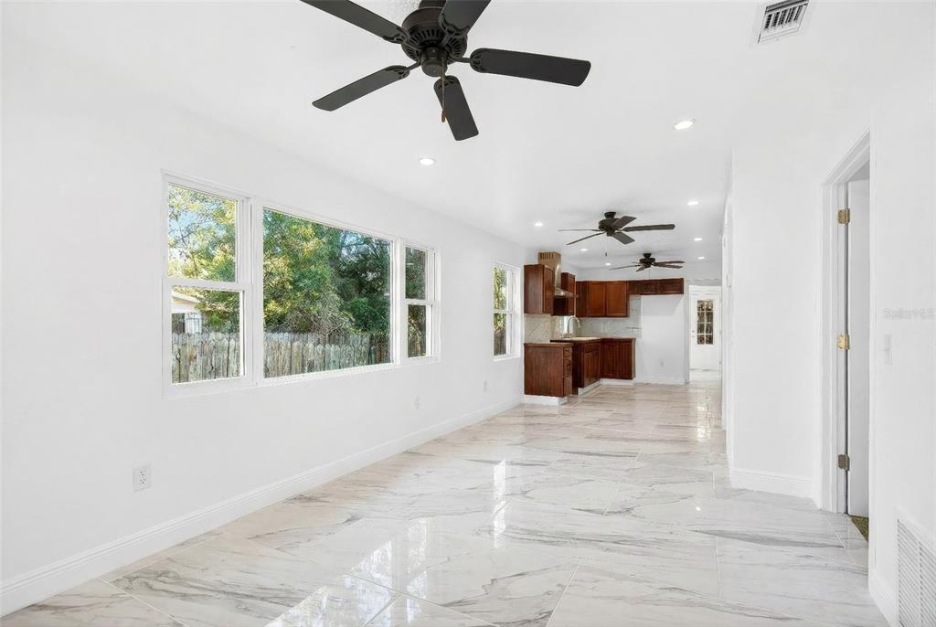 A bright room with white walls, marble-look tile flooring, and a kitchen in the background — 1110 SW FORT KING STREET, OCALA, FL