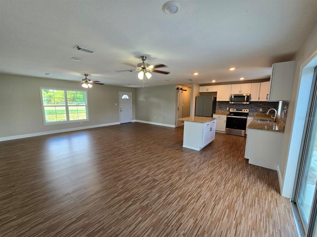An open-concept living area features wood-look flooring, a kitchen island, and white cabinetry — 11548 MISSOURI STREET, LEESBURG, FL