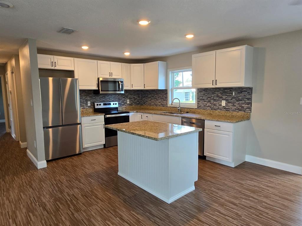 A kitchen features white cabinets, granite countertops, stainless steel appliances, and a central island — 11548 MISSOURI STREET, LEESBURG, FL