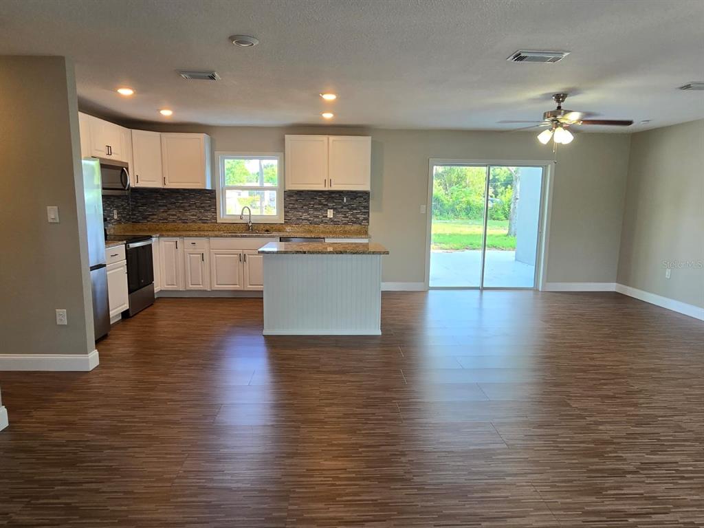 A kitchen with white cabinets, a center island, and wood-look flooring opens to a living area — 11548 MISSOURI STREET, LEESBURG, FL