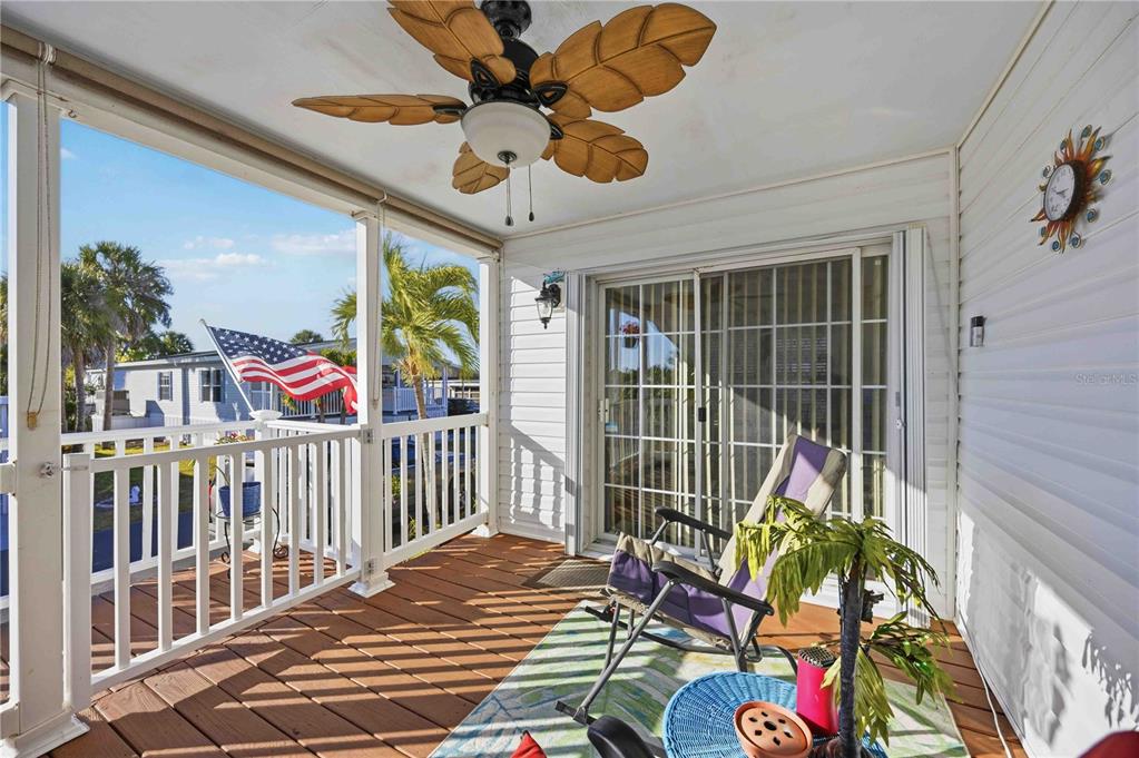A covered wooden deck features a leaf-shaped ceiling fan, white railings, and a sliding door — 10303 BURNT STORE ROAD UNIT 97, PUNTA GORDA, FL