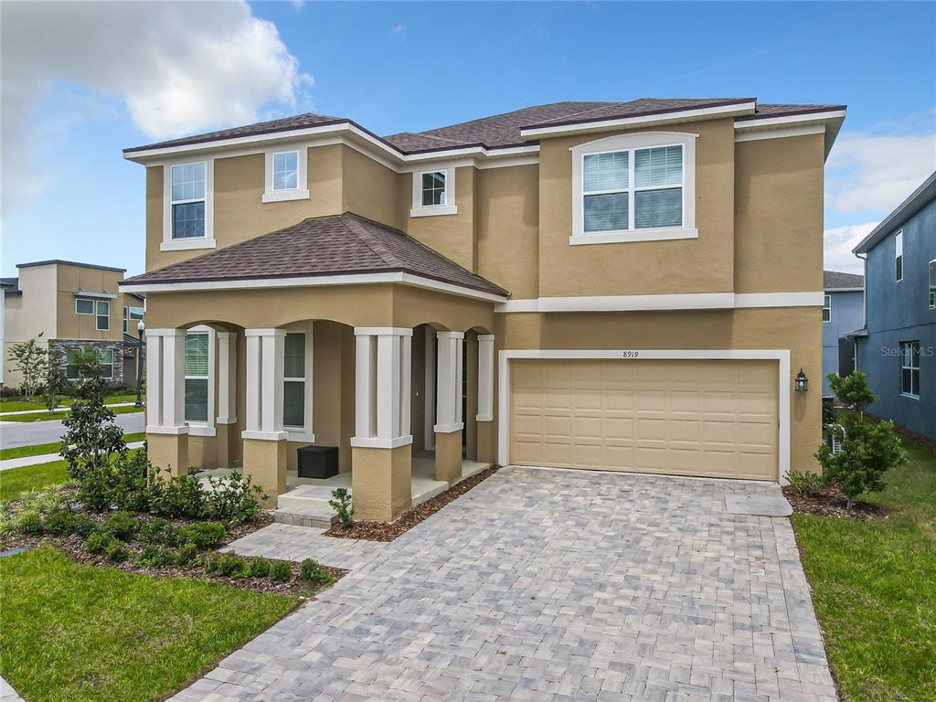 A two-story tan house features a covered front porch, a two-car garage, and a paver driveway — 8919 TROPICAL HAVEN COURT, KISSIMMEE, FL